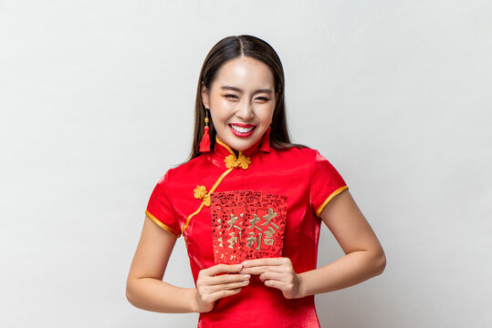Smiling happy Asian woman in traditional oriental costume holding red envelopes or Ang Pao in light gray background for Chinese new year concepts,  text means great luck great profit