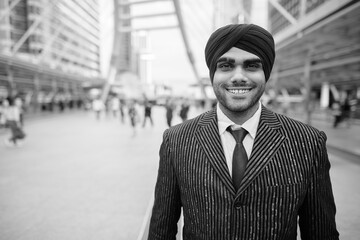 Happy young handsome Indian Sikh businessman wearing turban in the city