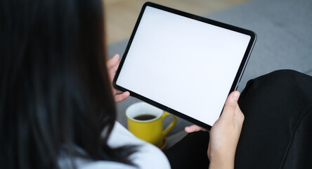 Close up view of casual young woman sitting on comfortable sofa and using digital tablet with blank screen.