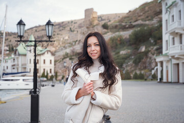 A woman in beige clothing enjoying the view of the sea on a warm, windy day.