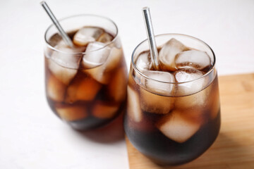 Glasses of tasty cola with ice cubes on white table, closeup