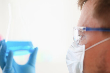 A portrait of a young surgeon chemist's doctor looks at a container with a blue liquid and a mask is fought with viruses and a vaccine for vaccines against diseases