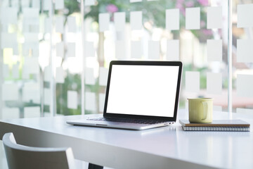 Mock up laptop computer with blank screen, coffee cup and notebook on modern workspace.