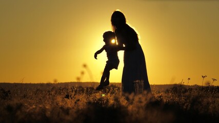 Fototapeta na wymiar Silhouette of a mother with a small child against the sunset sky. Happy motherhood life with daughter. A woman on maternity leave walks and plays with a baby. Kid soars in the air jumping high up