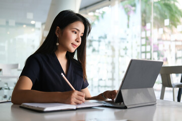 Portrait of happy young woman working on tablet pc while sitting at her working place in office.	