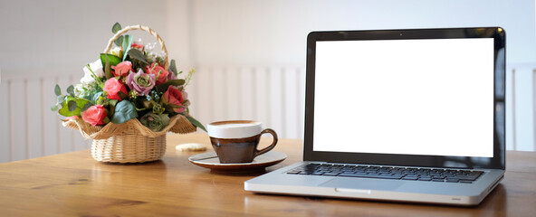 Mock up laptop computer with white screen, flowers and coffee cup on wooden table.White empty screen for advertise text.