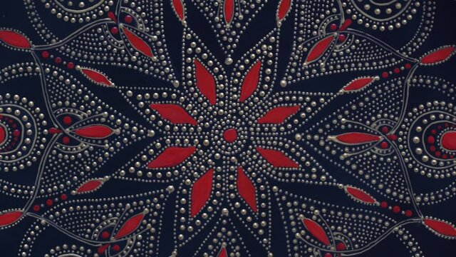 Decorative ceramic plate with black, red and golden colors, painted plate on background, closeup, top view, rotate. Decorative porcelain plate painted with acrylic paints, handwork, dot painting