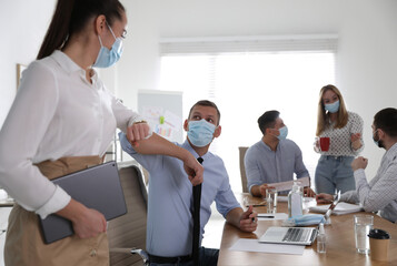 Coworkers with protective masks making elbow bump in office. Informal greeting during COVID-19 pandemic