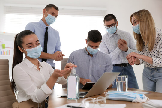 Coworkers with protective masks using hand sanitizer in office. Business meeting during COVID-19 pandemic