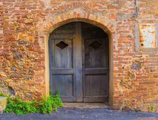 An old wooden door in a disused residential building in the historic centre of the medieval town of Monticiano in Siena Province, Tuscany, Italy
