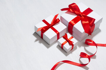 Minimalist elegant three New Year white gift boxes with red bow on white wood board as border.