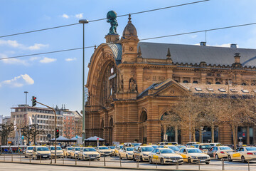 Historic building from the main train station in Frankfurt. Street with traffic lights and cars with a view of forecourt. Several taxis are waiting on the station forecourt - obrazy, fototapety, plakaty