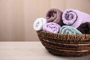 Fototapeta na wymiar Rolled soft towels in wicker basket on wooden table. Space for text