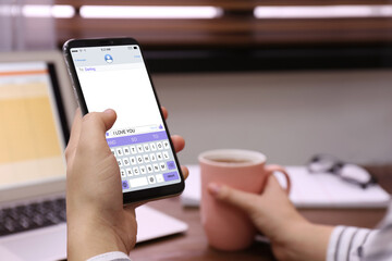 Woman sending message with text I Love You at table, closeup
