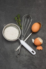 Sieve with flour, whisk, spoon with egg and egg shell