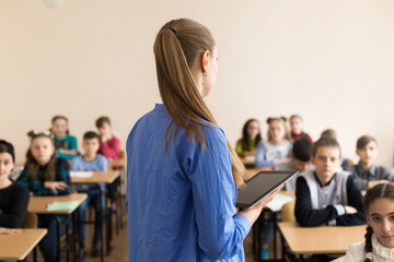 Teacher asking her students a question at the elementary school with tablet computer