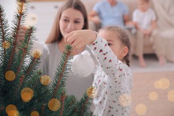 Mother with daughter decorating Christmas tree together at home, focus on hand