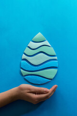 Woman hand holding paper cut water drop on blue background. Clean water and sanitation, saving water. World Water Day. Ecology concept.