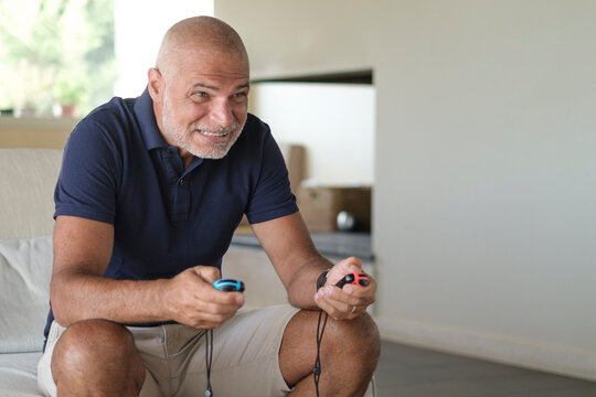 Uomo cinquantenne gioca ad un gioco elettronico nel salotto di casa