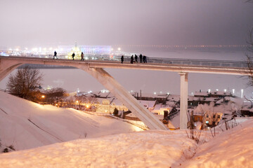 Nizhny Novgorod, Russia. January 5, 2021: Pedestrian bridge across the Sergievsky ravine on the background of the Arrow crossing the Oka and Volga in a winter evening. 