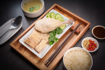 Steamed chicken and rice with spicy sauces and chicken soup, Hainanese chicken rice on a black table background, 