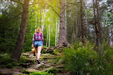Obraz premium Hipster girl in the mountains. Stylish woman in straw hat and checkered shirt in forest. Wanderlust concept. Freedom and psychology concept. Beautiful nature.