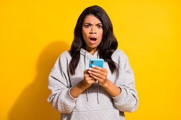 Photo of sad impressed dark skin woman wear grey hoodie chatting modern device isolated yellow color background