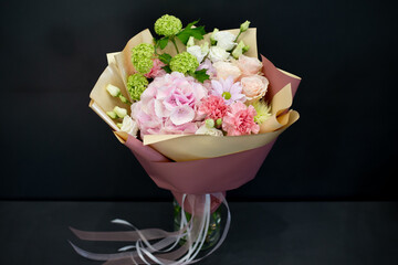 A bouquet of fresh flowers in decorative packaging. Photo on a dark background. Congratulatory bouquet.