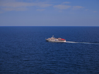 A large beautiful motor ship filled with people glides along the open blue sea to the horizon, leaving a trail of water behind it. Sea voyage on a summer day.