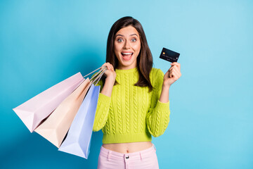 Photo portrait of excited girl holding shopping bags credit card isolated on pastel blue colored...