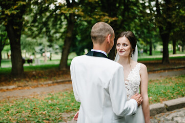 The bride and groom looking and standing in the park.