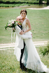 Bride and groom walking and holding bouquet of flowers and greens, greenery on nature. Romantic...