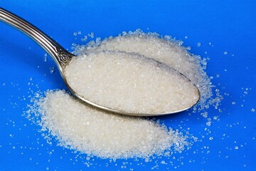 White sugar in a spoon. It is used in food products cookies and cakes, is added to drinks coffee, tea. The reason for excess weight, a lot of calories.