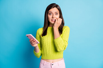 Photo of young girl afraid scared panic fail problem bite fingers use cellphone isolated over blue...