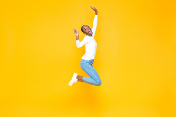 Fototapeta na wymiar Happy excited African American woman jumping with hands raising in yellow isolated studio background with copy space