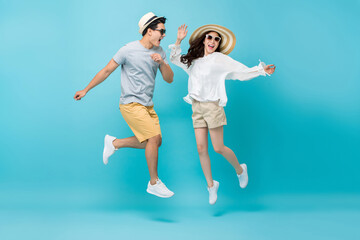 Smiling energetic Asian couple tourists in summer beach casual clothes jumping isolated on light blue studio background