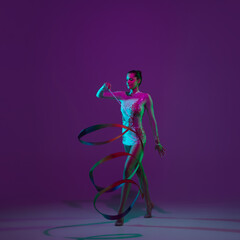 Motion. Young female athlete, rhythmic gymnastics artist dancing, training with tape isolated on purple studio background in neon light. Beautiful girl practicing with equipment. Grace in performance.