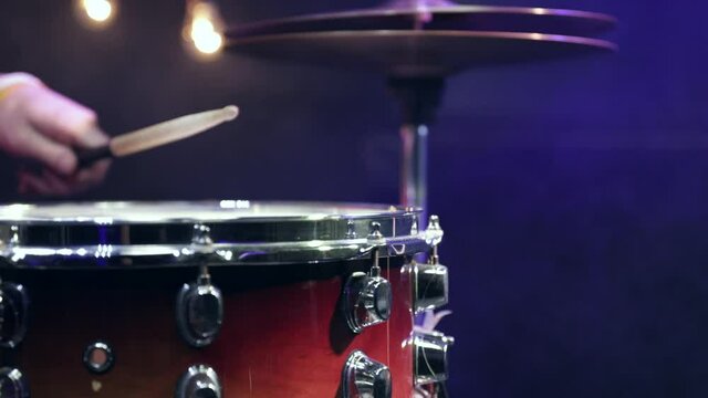 A man plays with sticks on a snare drum in a dark room with a beautiful light.