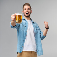 Young Man holding wearing jeans shirt holding glass of beer standing over Grey Background