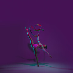 Vibrant. Young female athlete, rhythmic gymnastics artist dancing, training with tape isolated on purple studio background in neon light. Beautiful girl practicing with equipment. Grace in performance