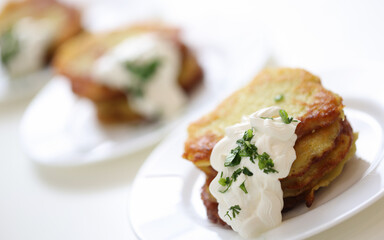 Many white plates with potato latkes and sour cream sauce are on table