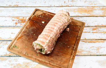 Preparation of a porchetta with a mixture of aromatic herbs placed on a piece of fresh pork belly open in the thickness