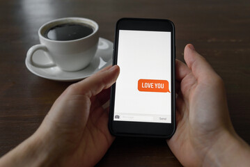 Hand holding phone with love valentine message from partner. Cup of coffee on table