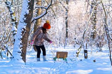 Fototapeta na wymiar child girl walks with sledge in the winter forest, bright sunlight and shadows on the snow, beautiful nature