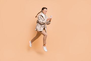 Fototapeta na wymiar Full size profile side photo of young happy positive girl running in air use smartphone isolated on beige color background