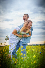 Young beautiful couple having fun on natural background. Date of guy and girl on a green field with glass and flowers in cloudy summer day. Yound family having rest together