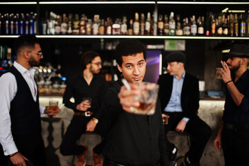 Stylish arab man against group of handsome retro well-dressed guys gangsters spend time at club, drinking on bar counter. Multiethnic male bachelor mafia party in restaurant.