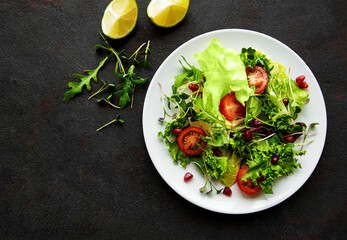 Fresh green mixed  salad bowl with tomatoes and microgreens  on black concrete background. Healthy food, top view.