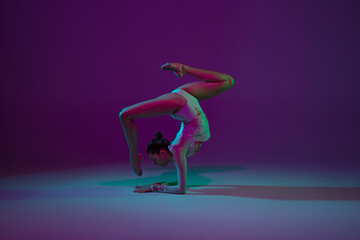 Aspiration. Young female athlete, rhythmic gymnastics artist dancing, training isolated on purple studio background in neon light. Beautiful girl practicing with equipment. Grace in performance.