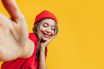 Close up of charming girl in red hat and red t-shirt making selfie on yellow background. Studio photo. Background for the inscription